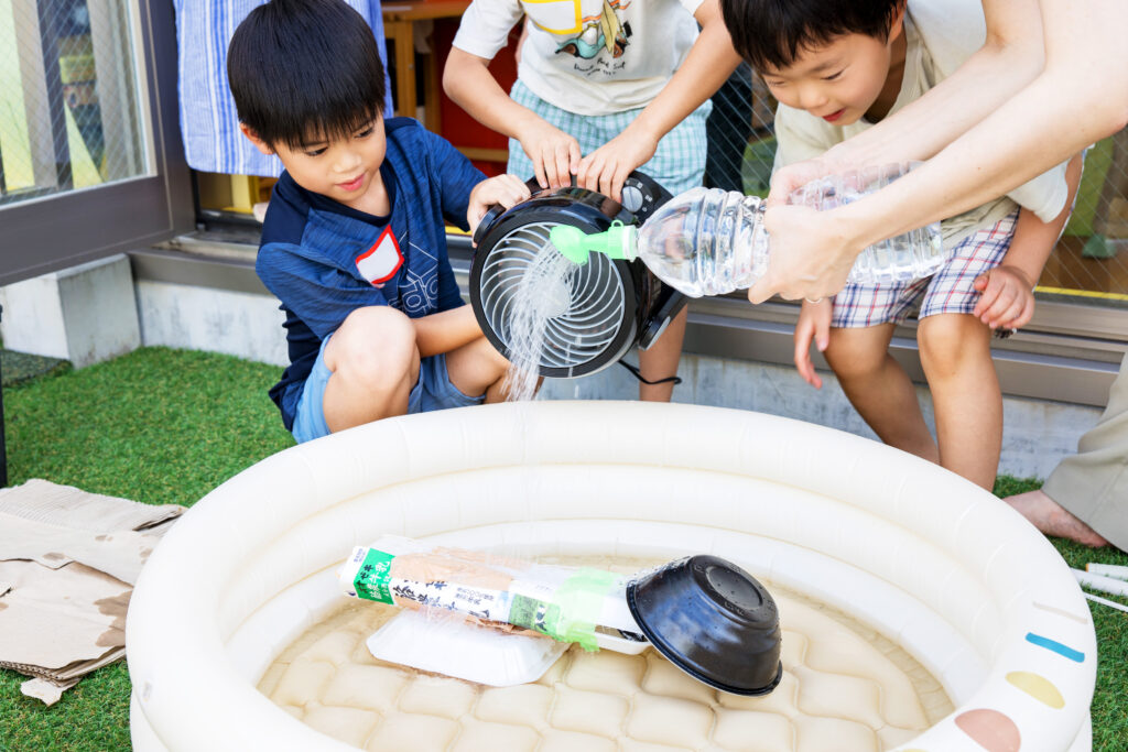 子どもたちが水を使った実験に挑戦。ペットボトルや扇風機を活用し、遊びながら科学を学ぶSTEAM教育の体験風景。