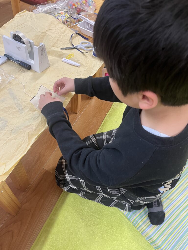 机に向かい、ハサミやテープを使って真剣に工作に取り組む男の子