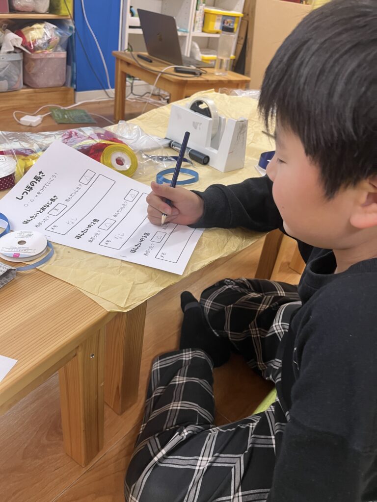 机に向かい、鉛筆を持ってワークシートに真剣に記入している男の子