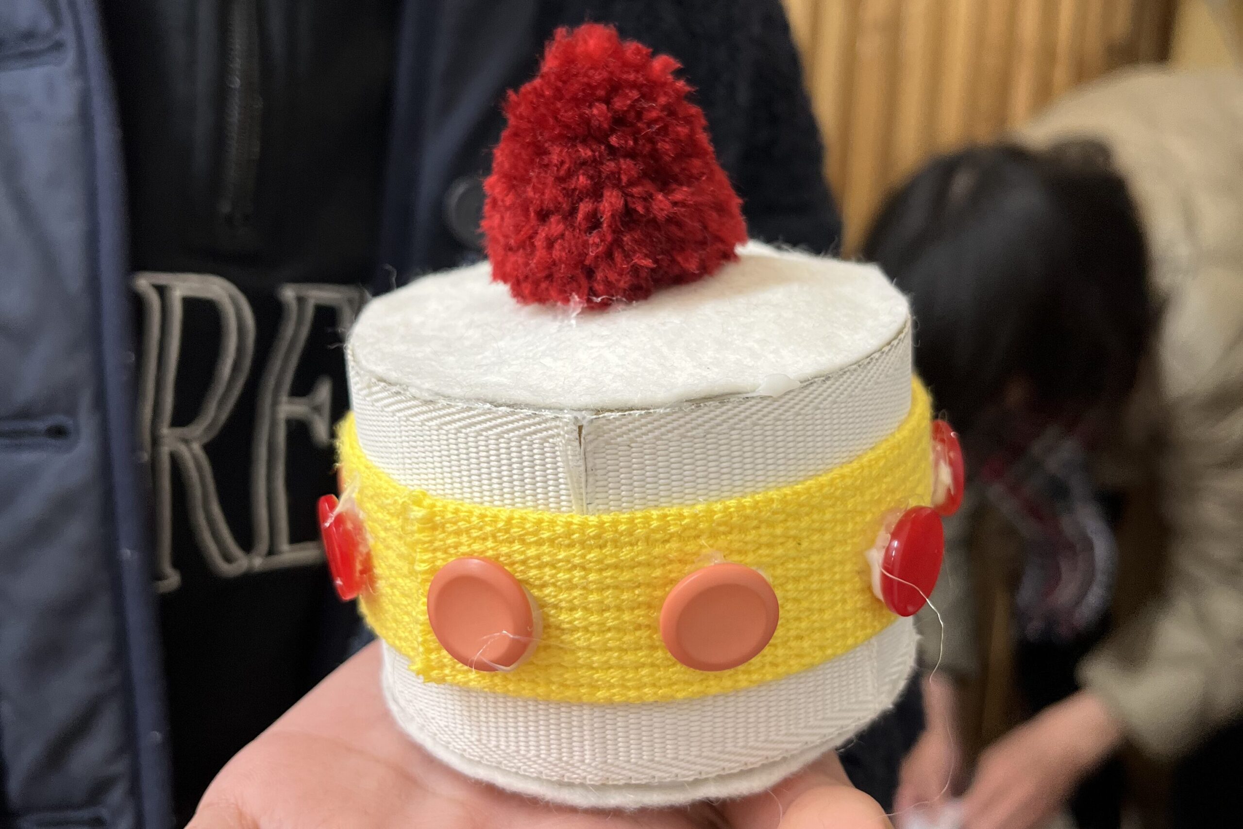 小学生が手作りしたケーキ風の工作作品を手のひらに乗せて見せている様子（STEAM工作教室）