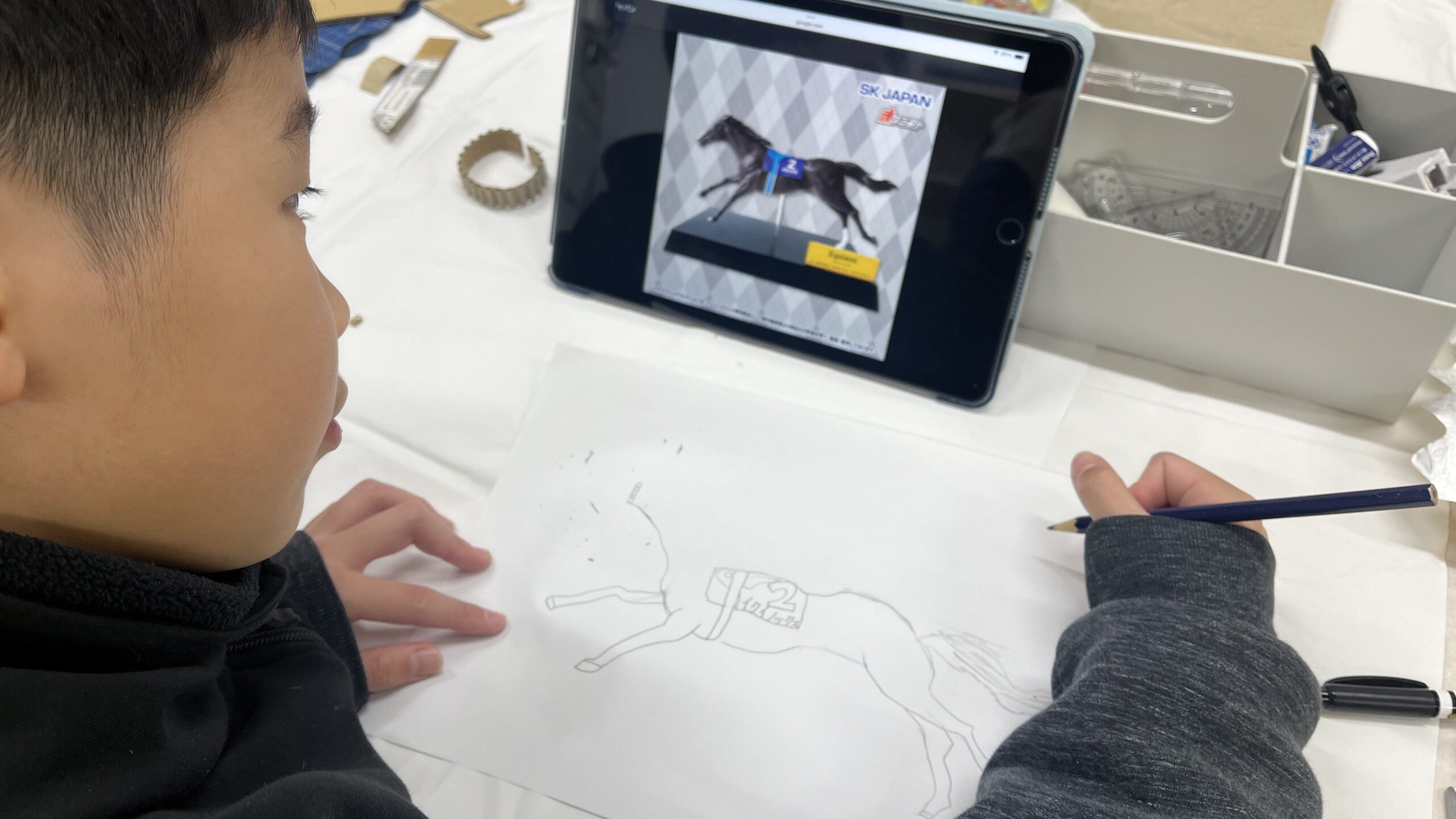 タブレットの画像を参考に、鉛筆でイクイノックスを描く男の子