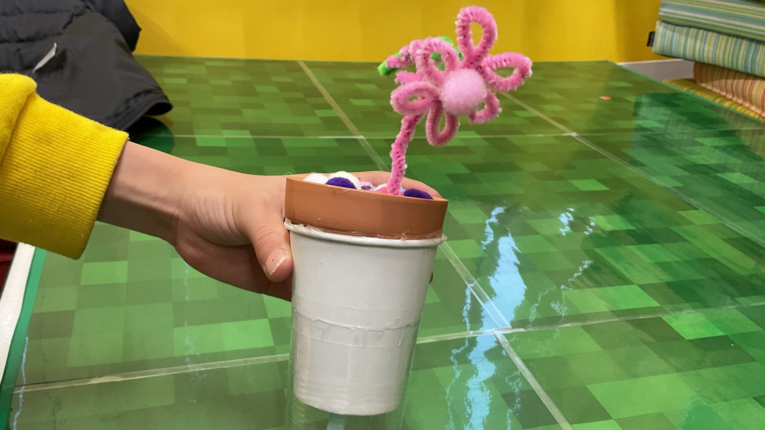 小学生男子がモールで作成したピンク色の花が手作りのプランターに植えられている。