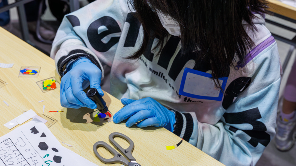 小学生が手袋を着けてUVレジンを流し込み、ボンボンドロップ風シールをぷくぷくに仕上げている制作の様子