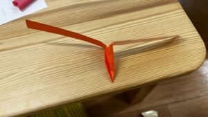 木のテーブルの上に置かれた、オレンジ色の紙で作られた手作りのペーパーヘリコプター（竹とんぼのような形）。