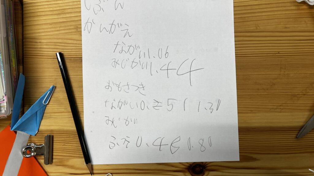 「じぶんのかんがえ」と題された、子供の手書きによる実験記録メモ。数値や「ながい」「みじかい」といった言葉が鉛筆で書かれており、横には記録に使用した鉛筆が添えられている。