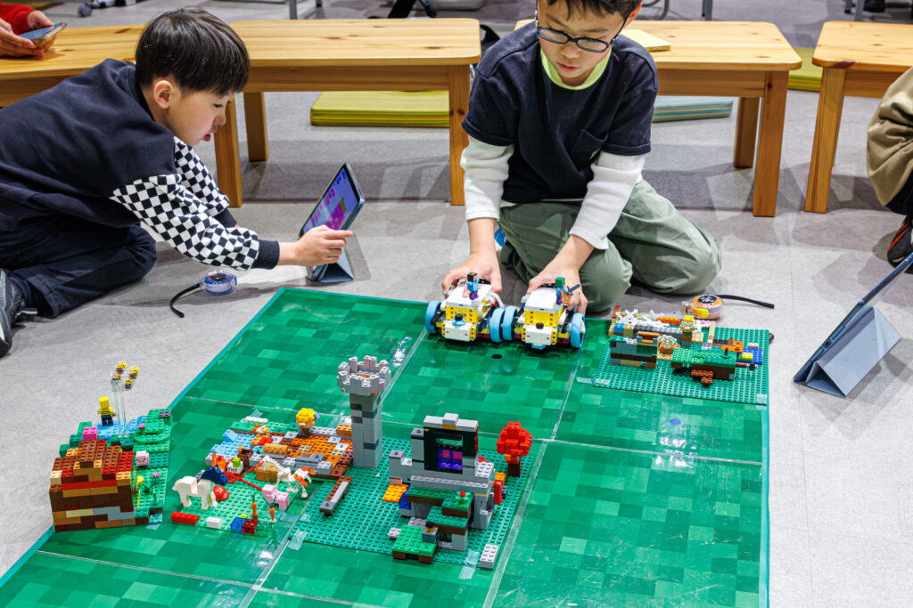 iPadを使ってレゴロボットを動かすためのプログラミングを組み立てる小学生