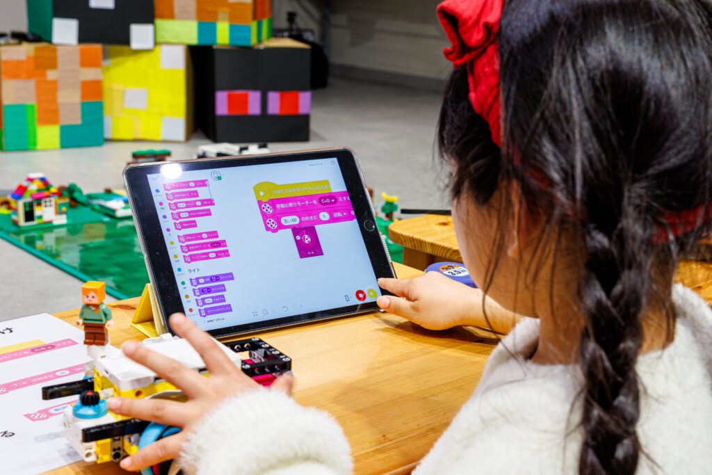 ミッテン府中のイベントで、iPadを操作してプログラミングを組み立てる女の子の後ろ姿