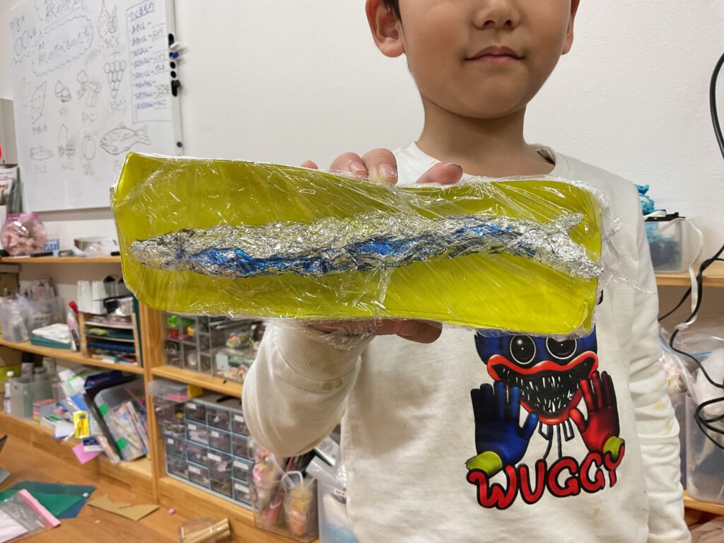 アルミホイルやラップなど身近な材料を使い、秋の味覚のさんまを再現した子どもの工作作品