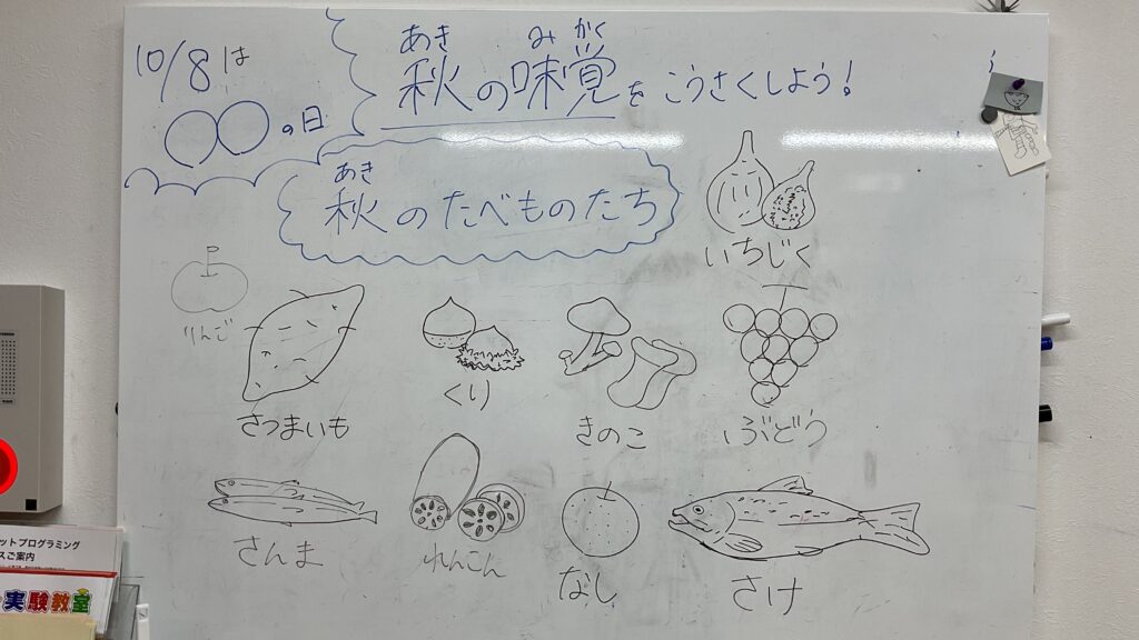 秋の味覚をテーマにした小学生向け工作教室のホワイトボード。さつまいもや栗、ぶどう、さんまなど秋の食べ物を紹介