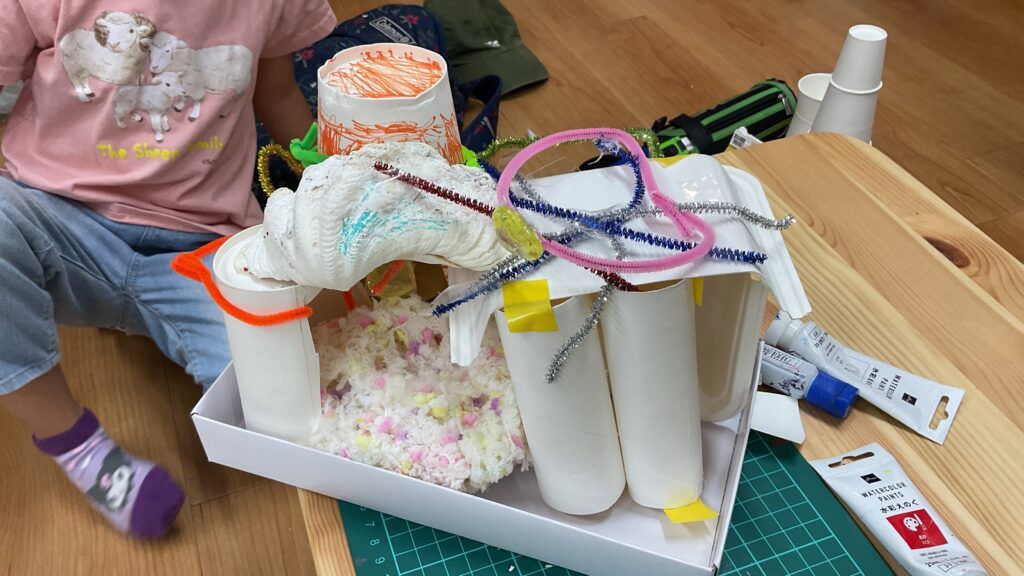 幼稚園児が、色付きモール、貝殻、トイレットペーパーの芯などで作った家。