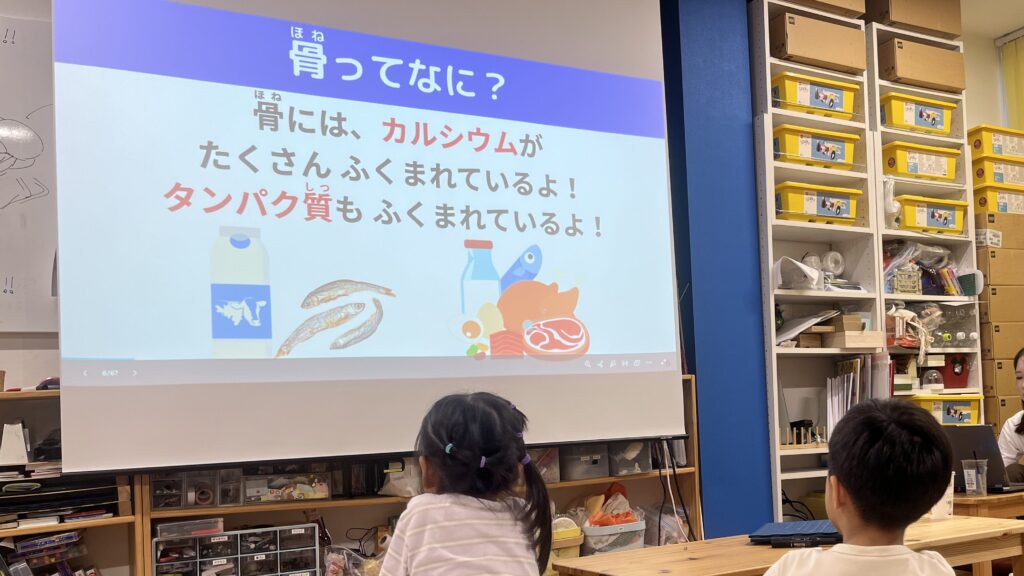 小学生向け実験教室において、スライドをとおして骨のしくみについて小学生が学んでいる様子。