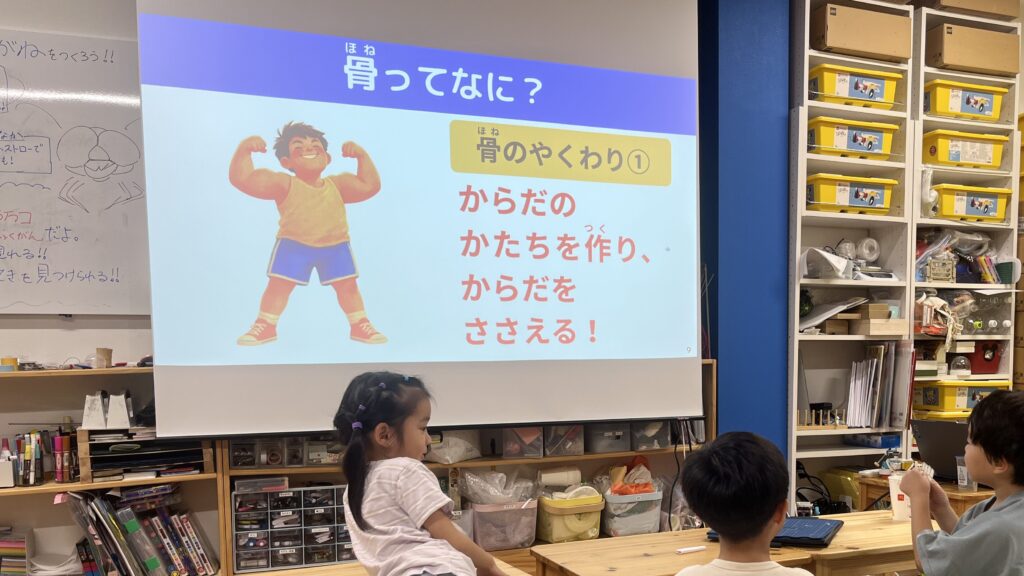 小学生向け実験教室において、スライドをとおしての骨の役割について小学生が学んでいる様子。