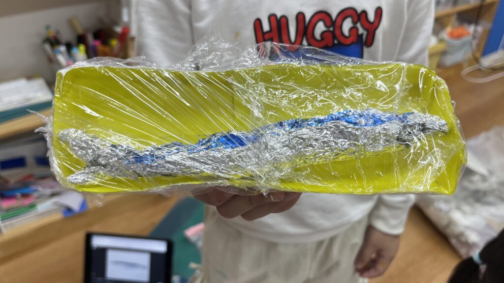 アルミホイルやラップなど身近な材料を使い、秋の味覚のさんまを再現した子どもの工作作品